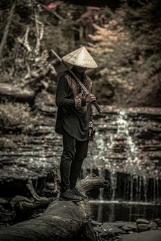 一个男人穿着传统武士服装，站在瀑布旁，手持一把剑