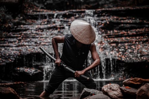 Free A powerful image of a samurai warrior in traditional attire, standing by a waterfall with a sword. Stock Photo