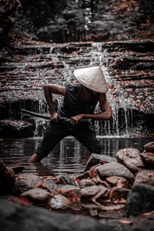 Free A man in traditional attire poses with a sword in a serene waterfall setting. Stock Photo