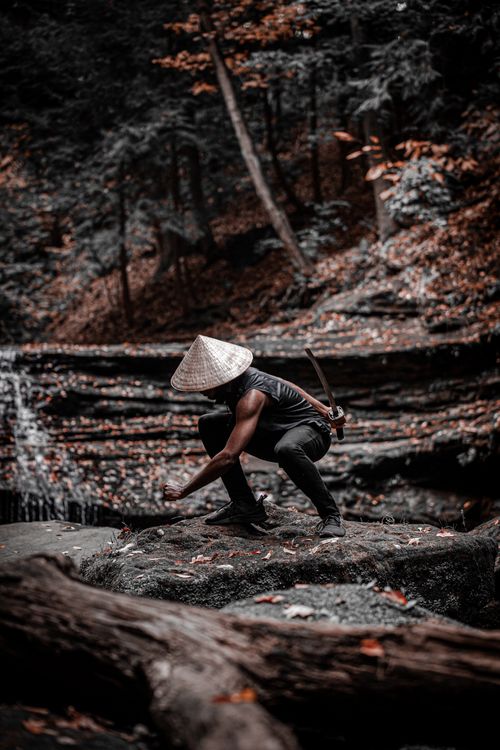 Free A warrior wearing an Asian conical hat in a forest with a sword, evokes an ancient samurai style. Stock Photo