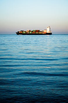 Serene view of a cargo ship transporting containers across a calm blue ocean under a clear sky.