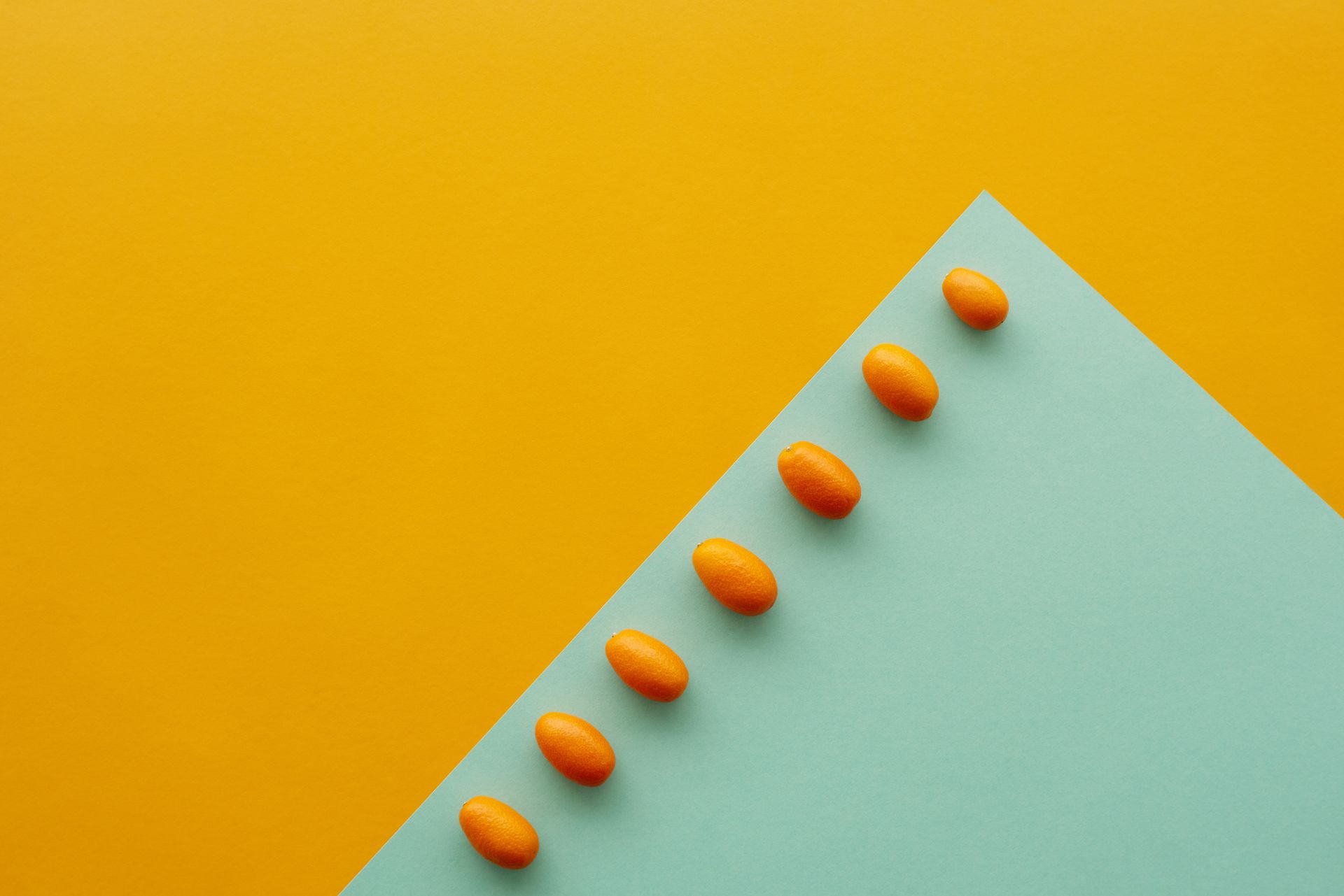 Kumquats aligned on a vibrant yellow and teal background with ample copy space.