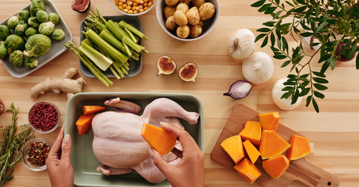 Hands preparing chicken with fresh vegetables on a wooden table.