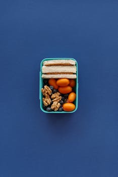 Vibrant lunchbox featuring walnuts, blueberries, mandarins, and sandwiches on a blue background.