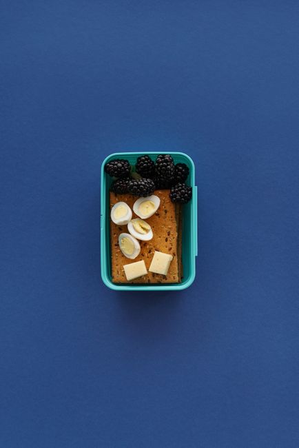 Top view of a healthy lunchbox with crackers, bananas, and blackberries on a blue background.