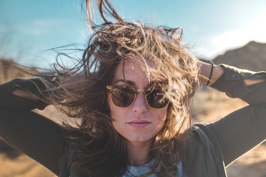 阳光明媚的户外，一位戴着太阳镜、秀发随风飘扬的女性肖像，尽显风格与自信