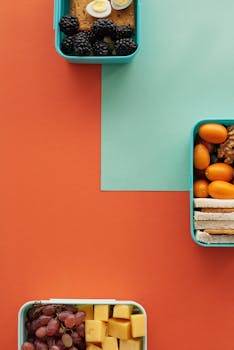 Top view of various lunch boxes with fruits and snacks on a vibrant background.