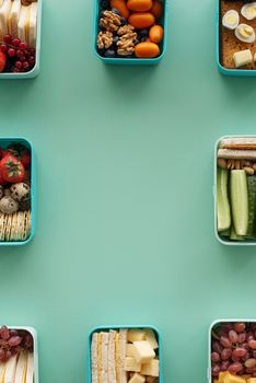 Top view of assorted fresh snacks in containers on green background.