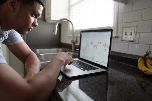 Focused man examining financial graphs on a laptop in a modern kitchen setting.