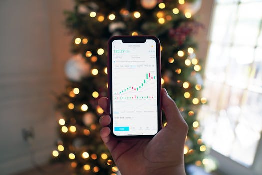 Close-up of a smartphone displaying stock market trading app with a background of Christmas lights.