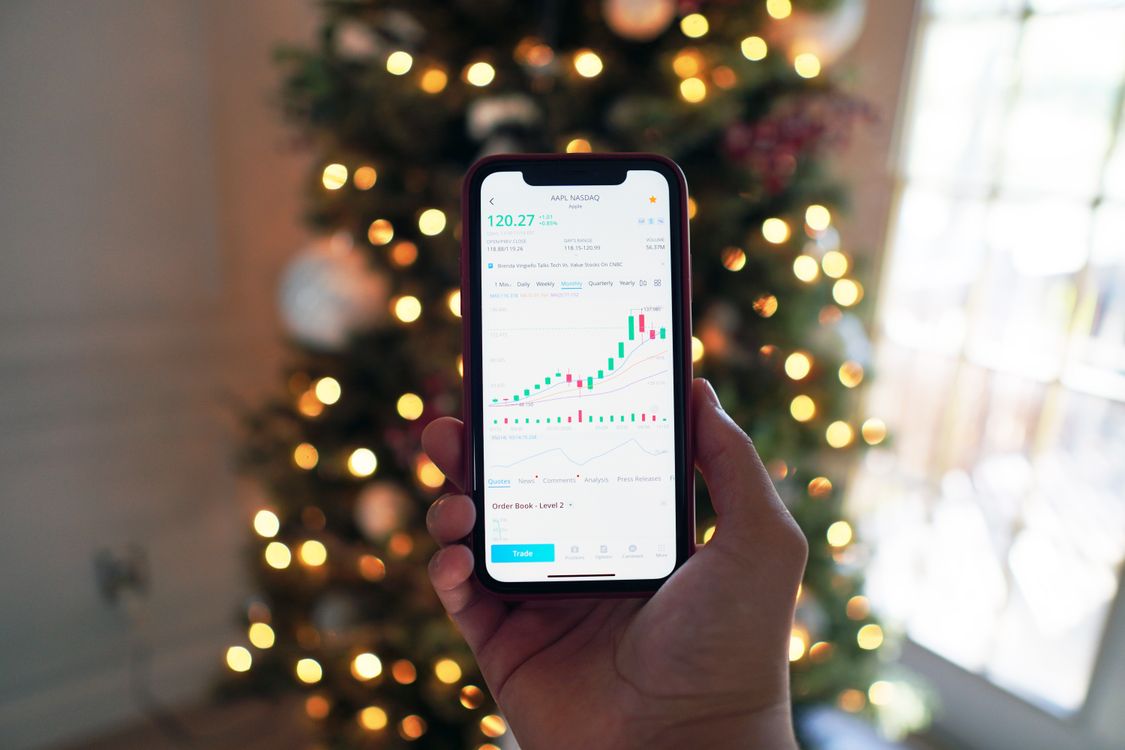 Free Close-up of a smartphone displaying stock market trading app with a background of Christmas lights. Stock Photo