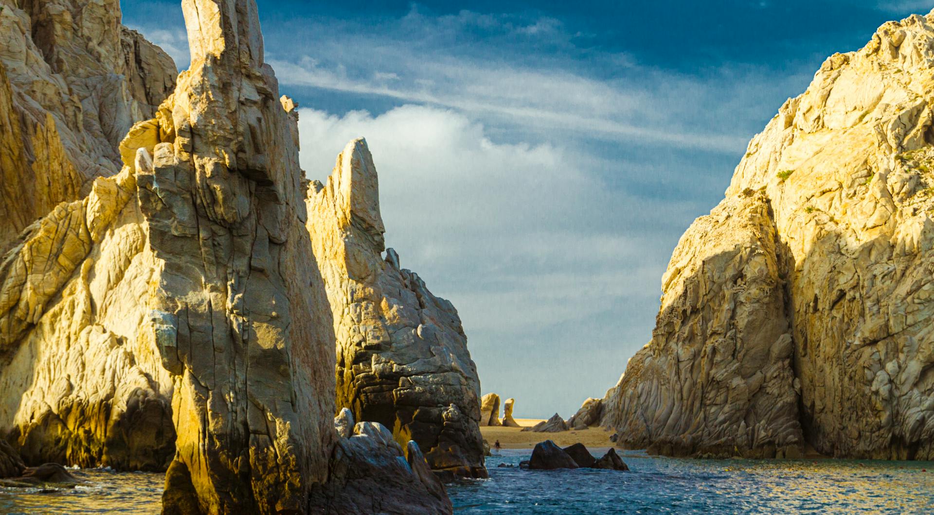 Dramatic rock formations at Cabo San Lucas coast under a vibrant sky.