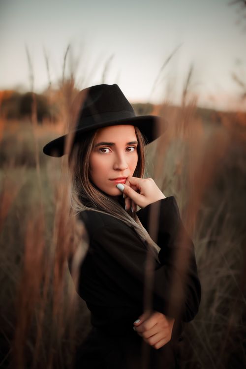 Free A fashionable woman poses outdoors in a black coat and hat, surrounded by nature's earthy tones. Stock Photo