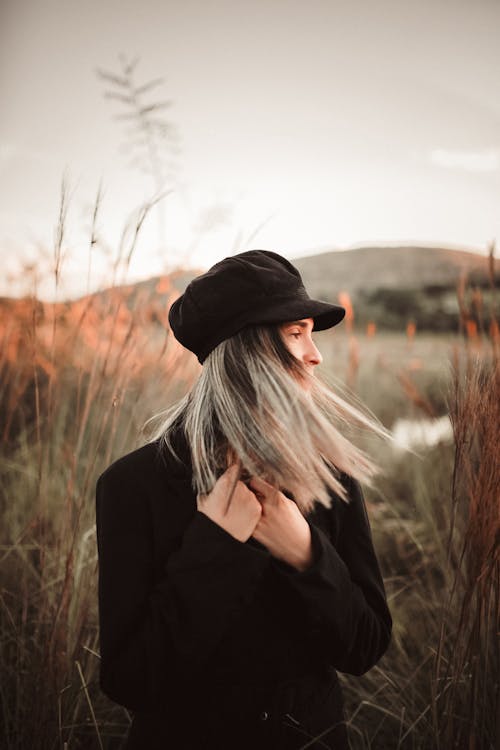 茶色の芝生のフィールドに立っている黒い長袖シャツと黒い帽子の女性