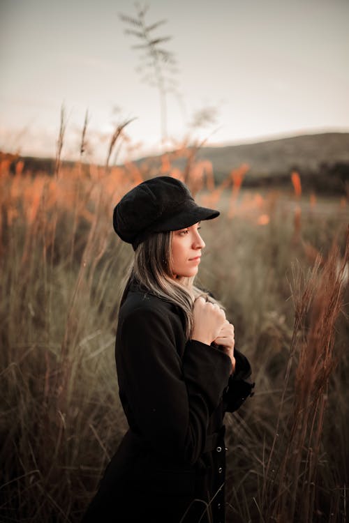 Woman in Black Coat and Cap Standing on Brown Grass Field