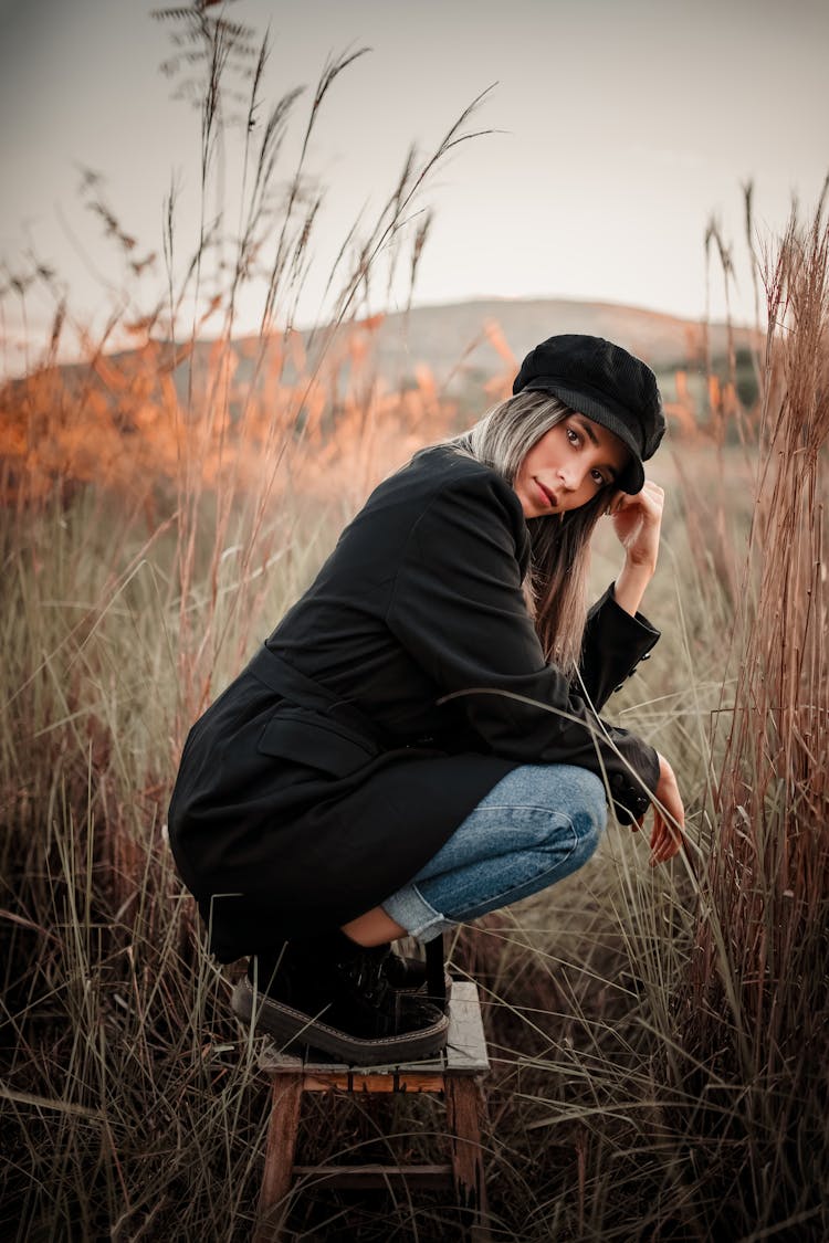 Woman In Black Coat And Blue Jeans Squatting On Stool