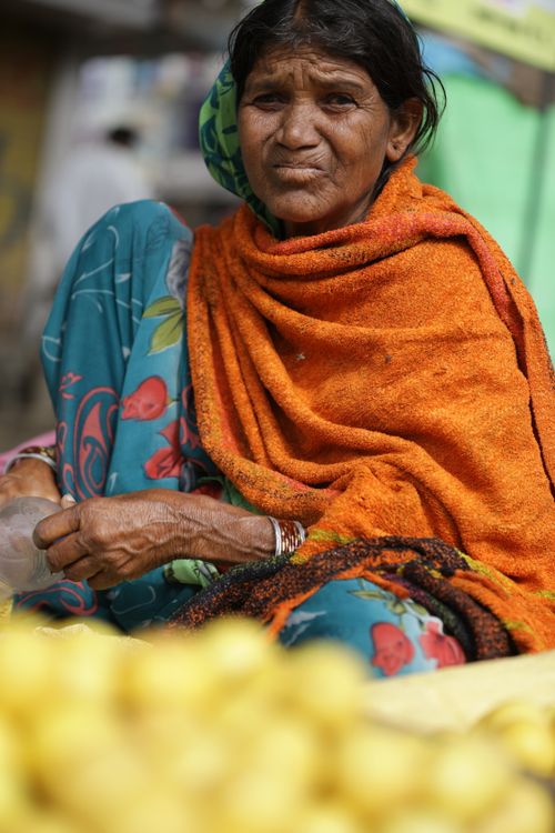 Free Elderly woman in colorful attire sitting at a fruit market stall with an array of lemons in the foreground. Stock Photo