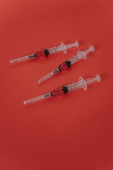 Close-up of three syringes with red liquid on a red surface, medical theme.