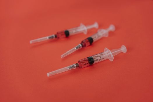 在一个大胆的红色表面上，有三个装着红色液体的注射器，呈现出医疗主题