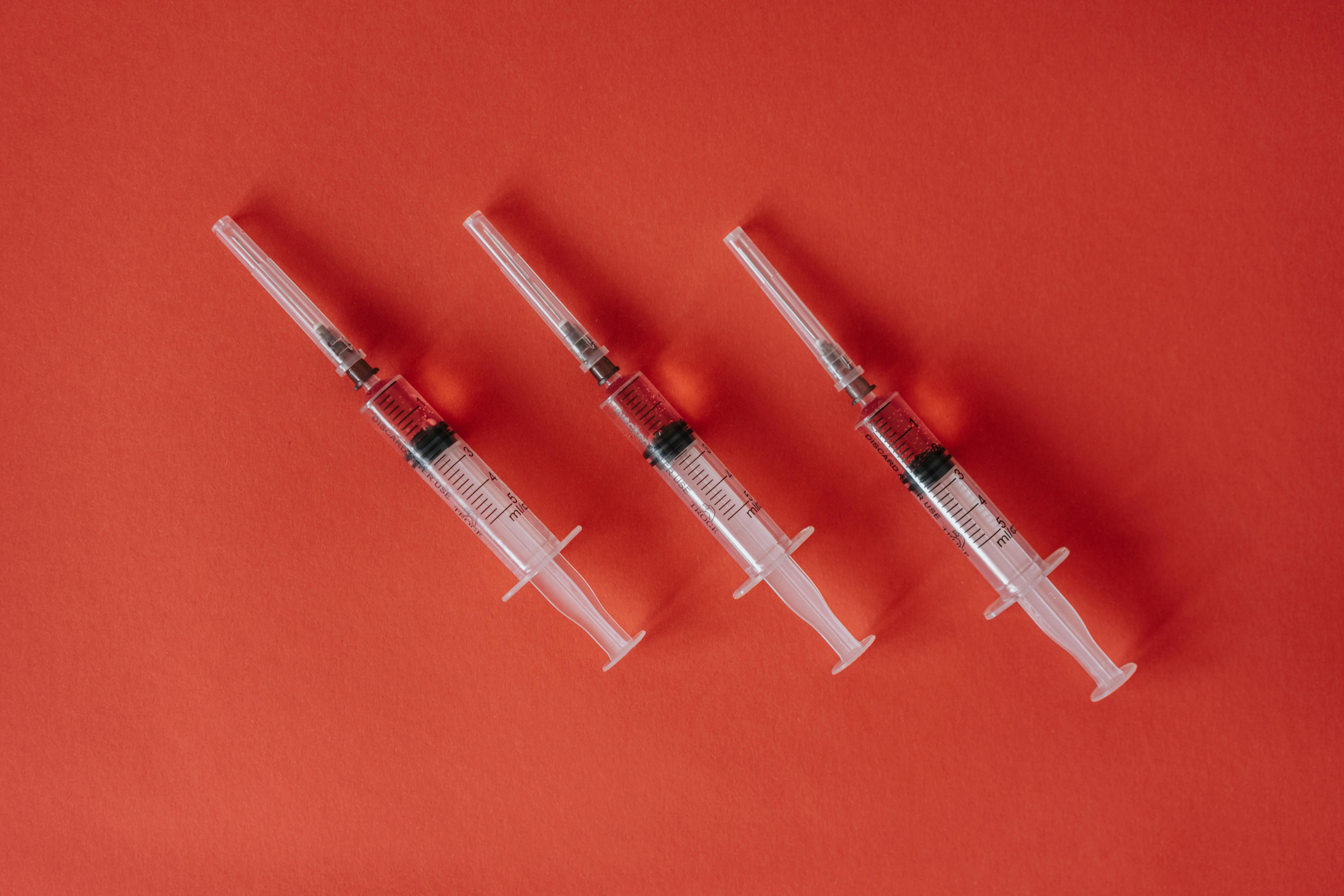 Three syringes arranged on a red surface showcasing medical equipment with copy space.