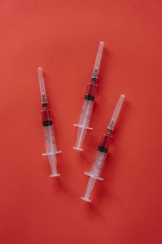 Close-up of three syringes arranged on a vibrant red background, ideal for healthcare themes.