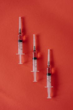 三个注射器置于生动的红色背景之上，突显医疗保健主题