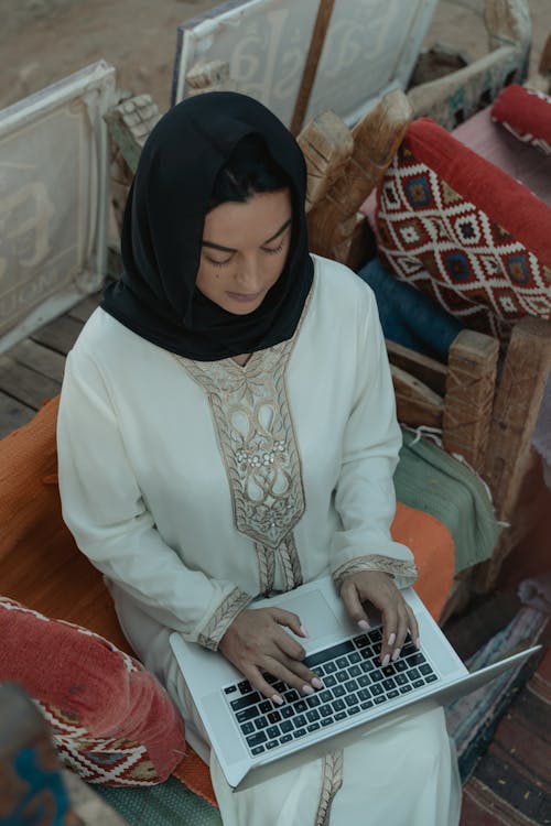 Woman in White Long Sleeve Dress and Black Hijab Sitting on Chair