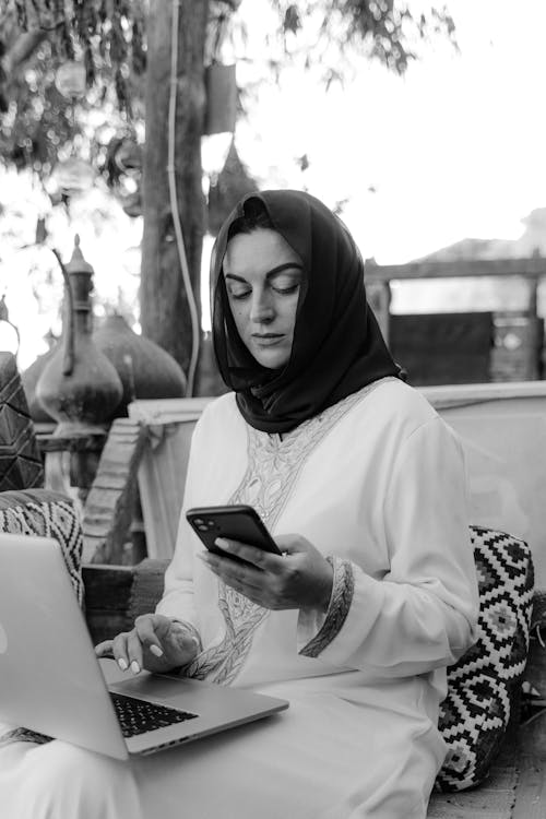 A Grayscale of a Woman in a Hijab Using a Smartphone