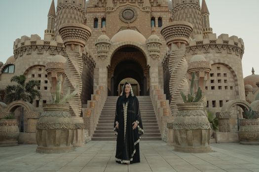 Woman in traditional black robe standing before an ornate architectural castle, showcasing cultural heritage.