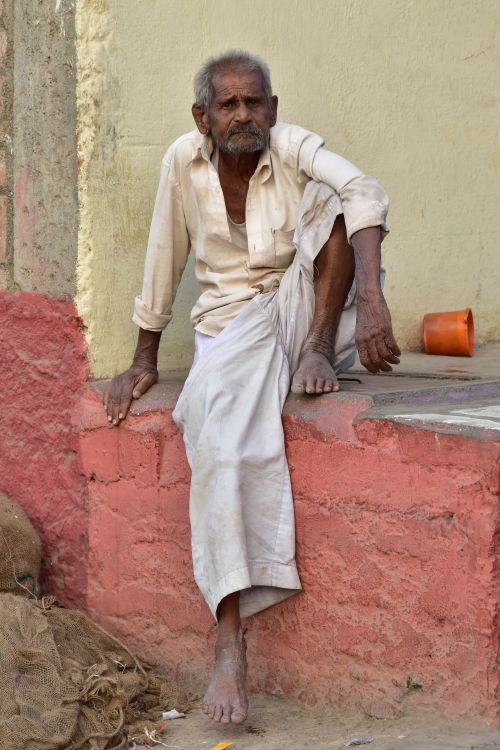 Free An elderly Indian man sitting outdoors against a colorful wall in Pune, India. Stock Photo