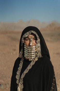 身着传统贝都因人服装和硬币珠宝的女人出现在沙漠景观中