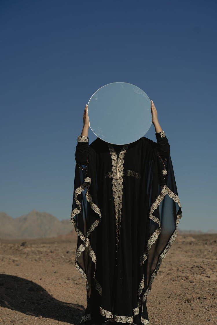 A Woman Wearing A Black Robe Holding A Mirror