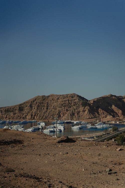 Free A tranquil marina in a desert setting with yachts against rocky hills under a blue sky. Stock Photo