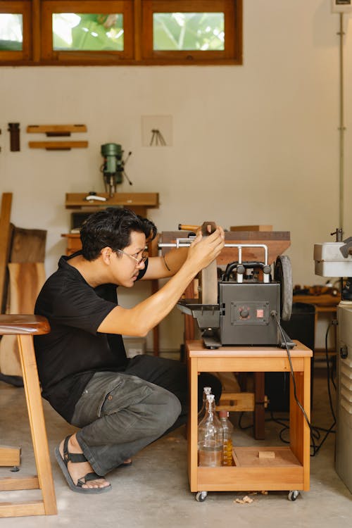 Side view of young attentive ethnic male woodworker using grinding machine while working with wooden block in workshop