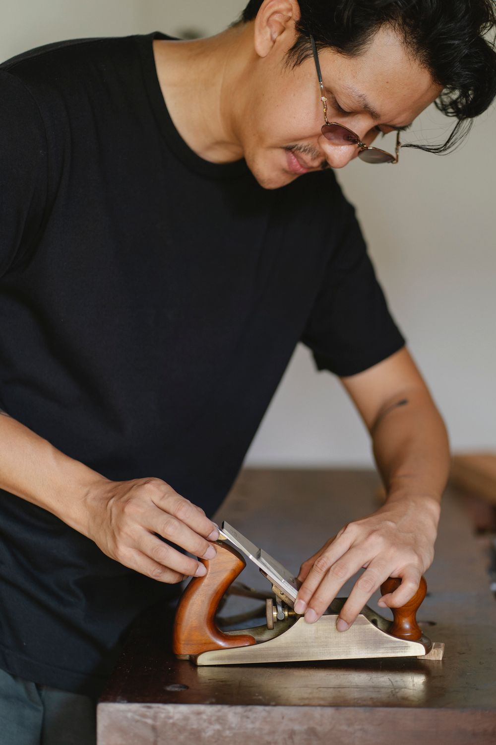 A craftsman's hands guiding a hand plane over a walnut board, curls of shavings rising