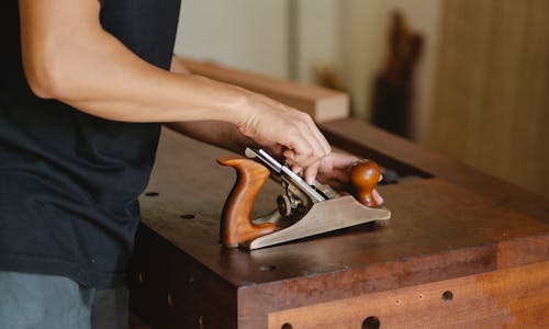 Side view of unrecognizable male carpenter changing knife in planer while cutting piece of board in studio on blurred background