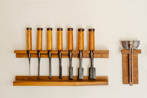 Free Collection of metal chisels with wooden handles and wood cutters for woodwork arranged on shelf on white wall in workshop Stock Photo