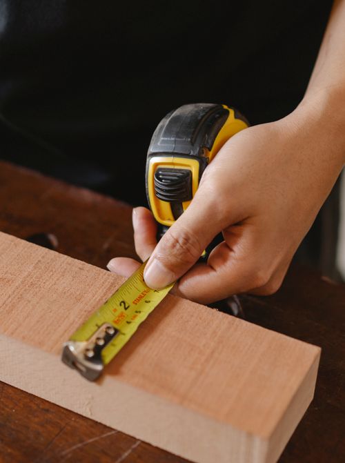 Free Unrecognizable male carpenter with special ruler measuring width of wooden board while working in professional studio at workbench Stock Photo