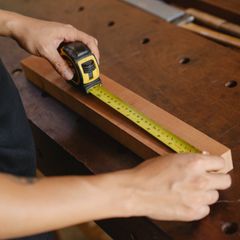 Measuring a length of wood on a workbench with a yellow and black tape measure