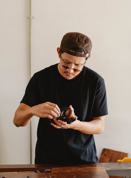 Concentrated male master wearing eyeglasses standing at table with special instrument for woodwork in hands while working in studio against white wall