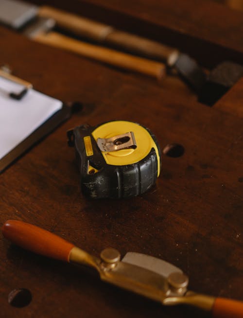 Special yellow ruler placed on wooden workbench near professional tools with joinery instruments for carpentry near clipboard in workshop on blurred background