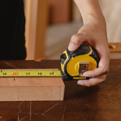 A hand holding a yellow and black tape measure against a block of wood