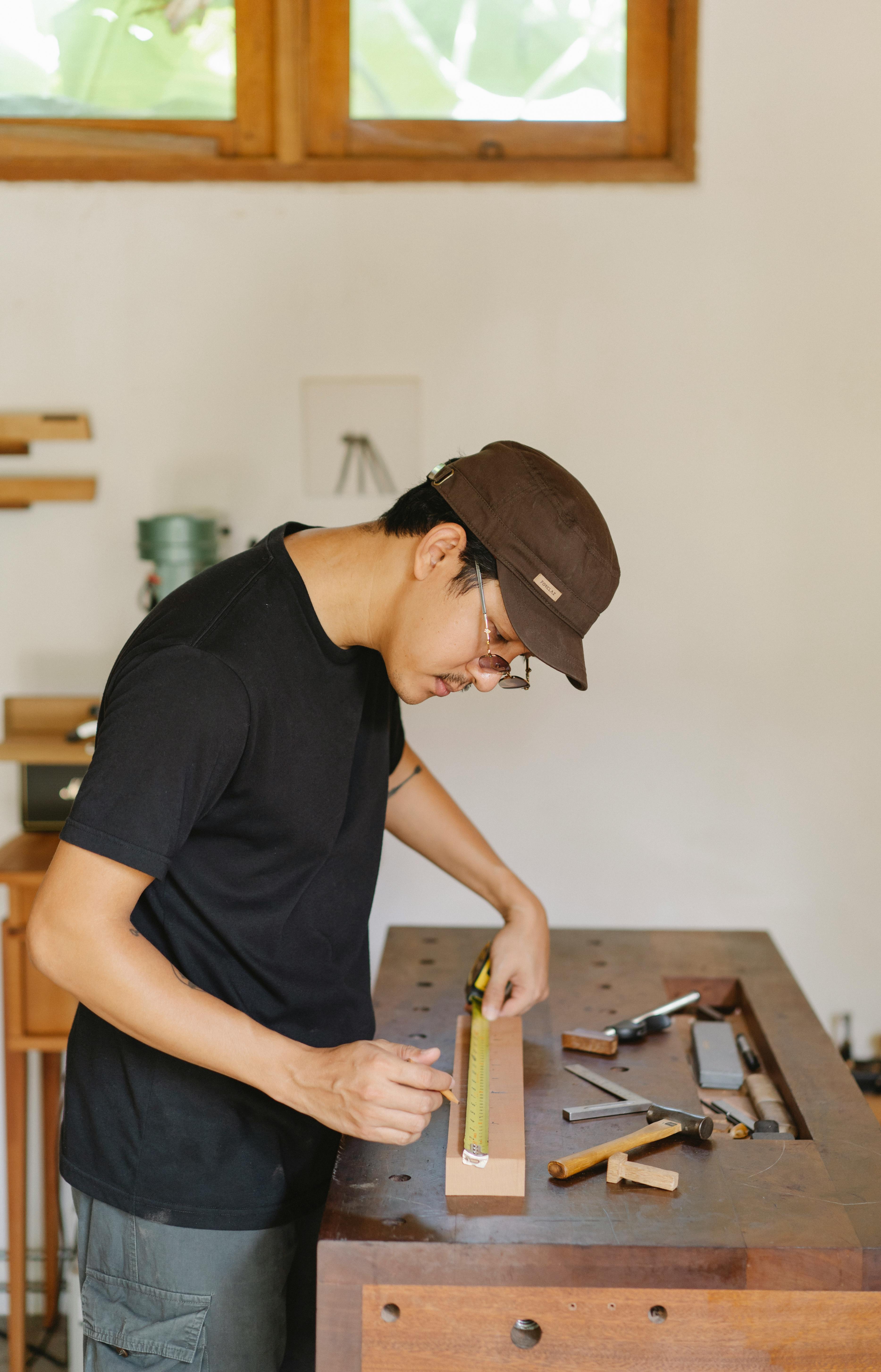 ethnic carpenter measuring wooden plank in workshop