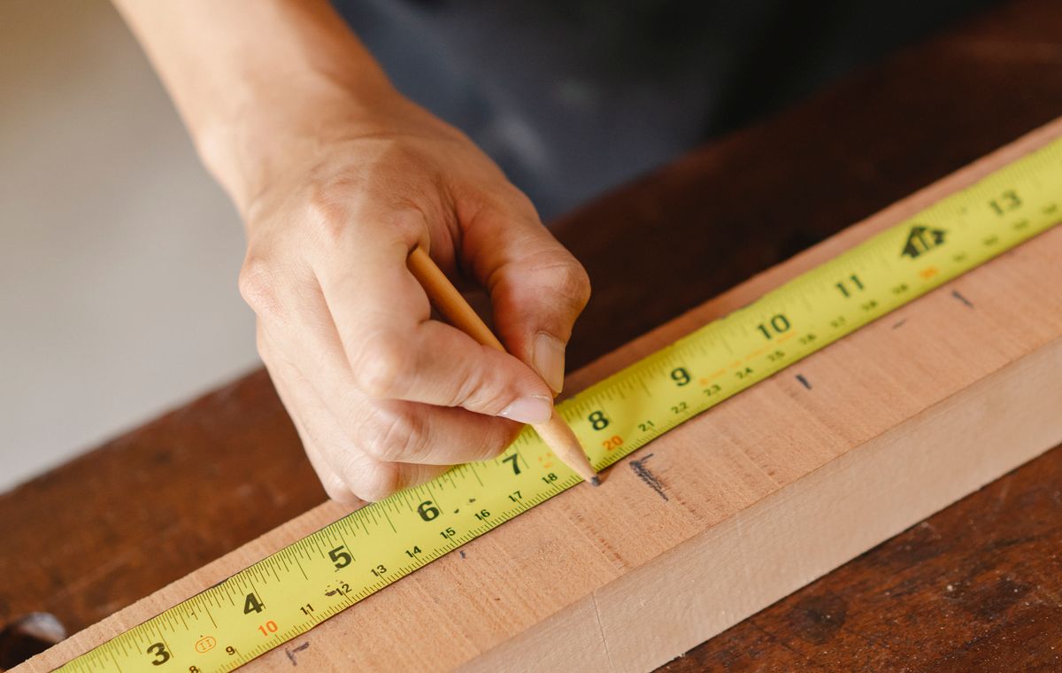 Builder marking a wooden plank with a measuring tape