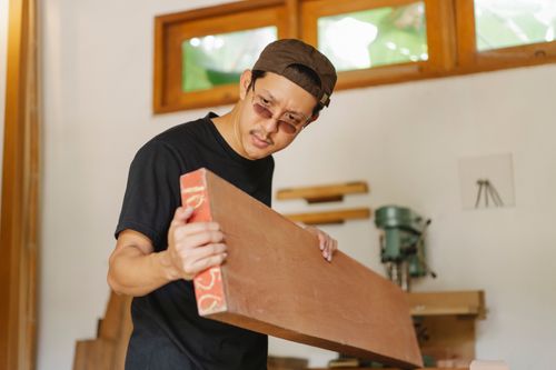 Free Serious concentrated joiner in eyeglasses and T shirt carrying timber plank in workshop Stock Photo