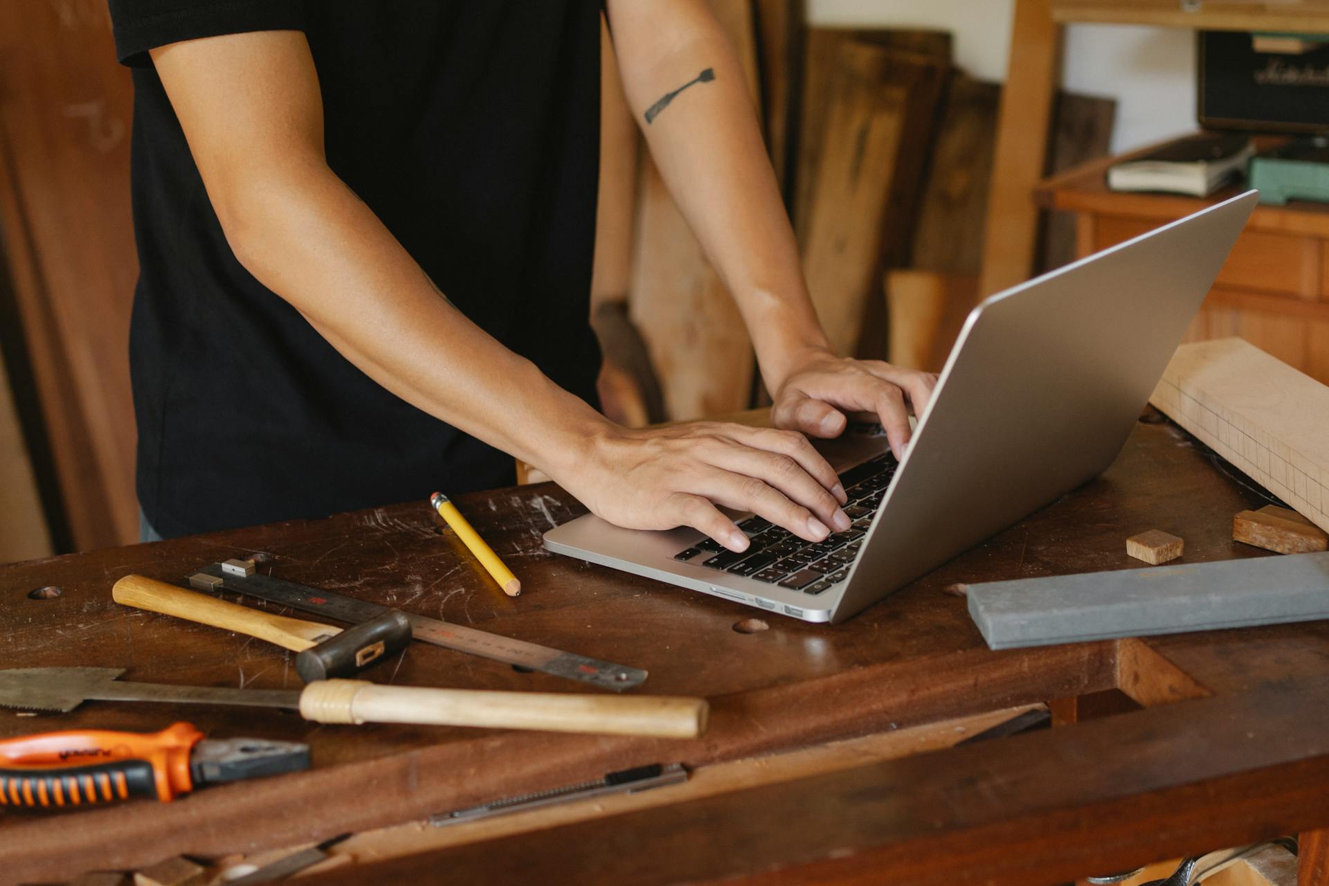 Crop anonymous male searching information on internet on wooden table among carpentry tools in workshop