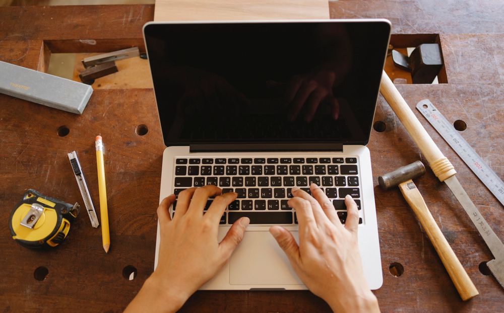Hände tippen in einer Werkstatt zwischen Werkzeug auf dem Laptop