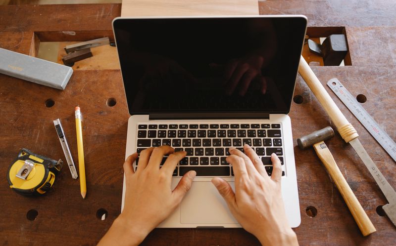Hände tippen in einer Werkstatt zwischen Werkzeug auf dem Laptop