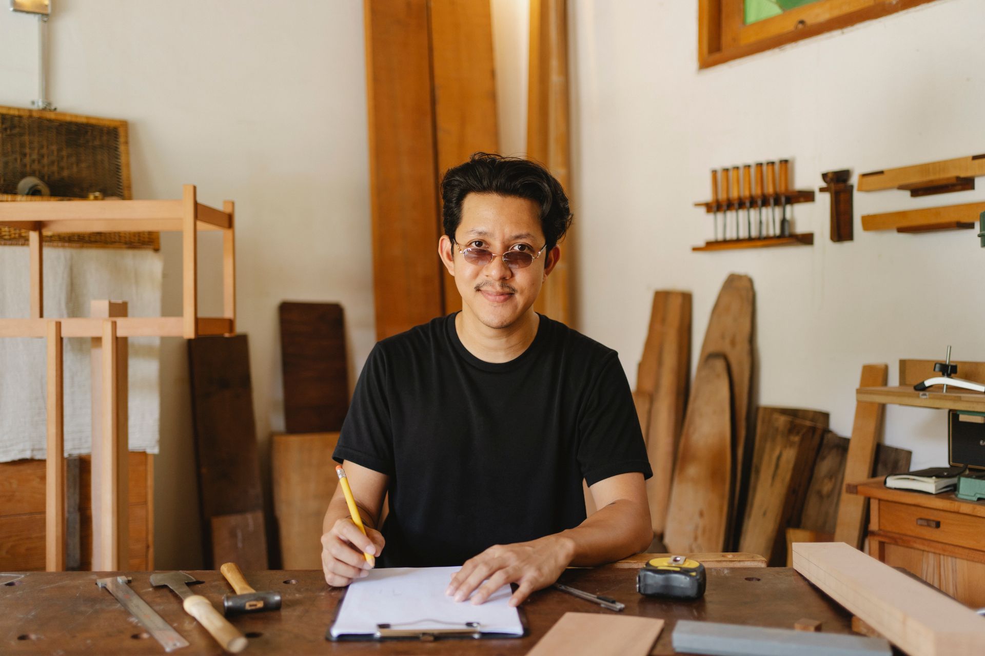 Confident carpenter in glasses working on project plans in a workshop setting. Tools and creative atmosphere.