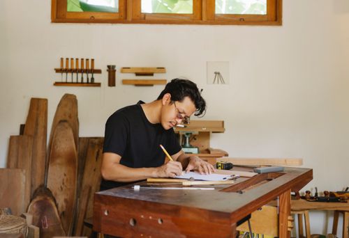 Free Serious Asian male master sitting at wooden table and creating new design on paper Stock Photo
